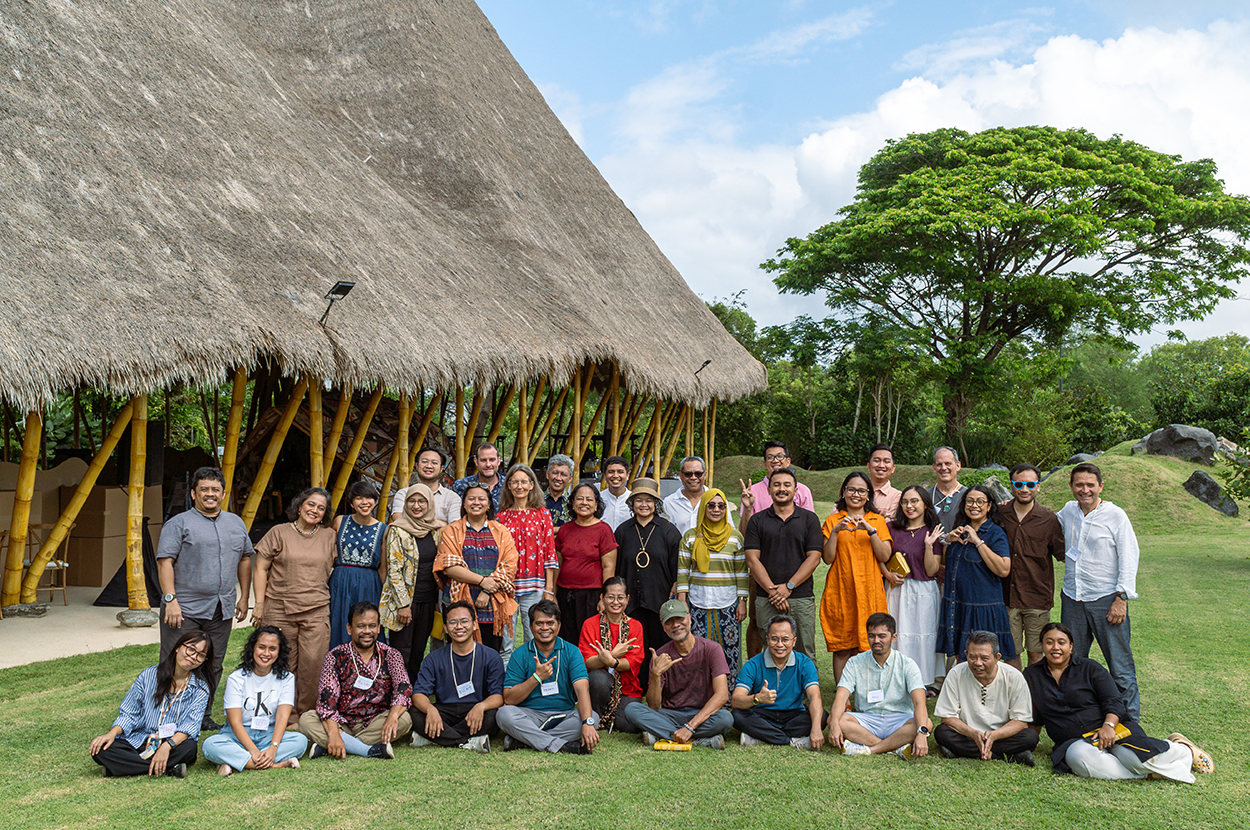 A group of people stand in front of a bamboo structure in a green landscape.
