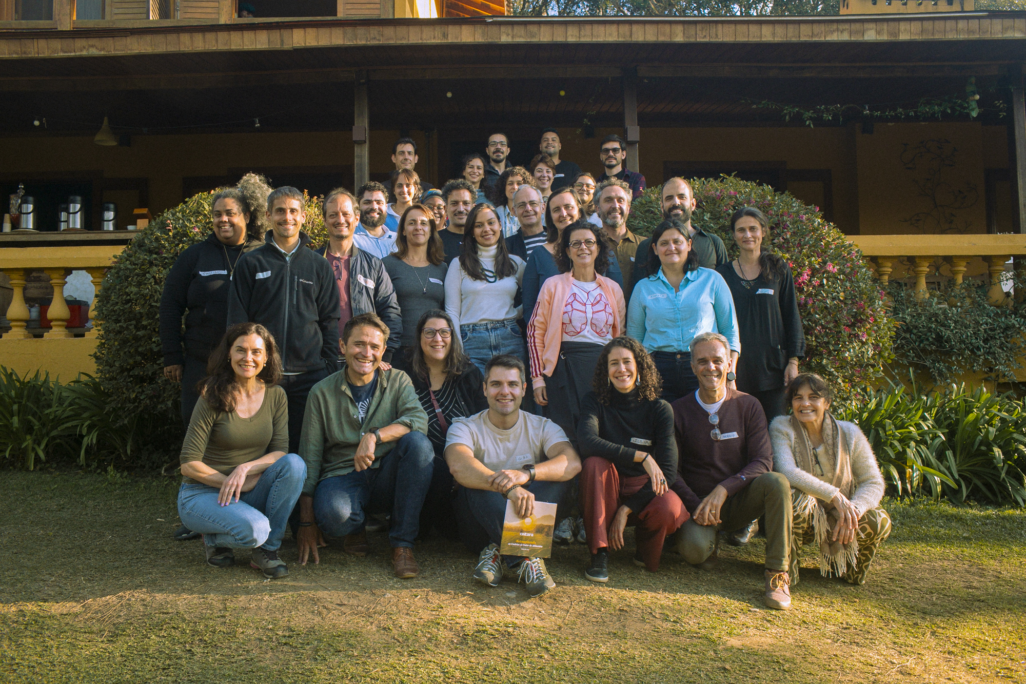 A diverse group of people stand in front of an eco-lodge on a grassy spot.
